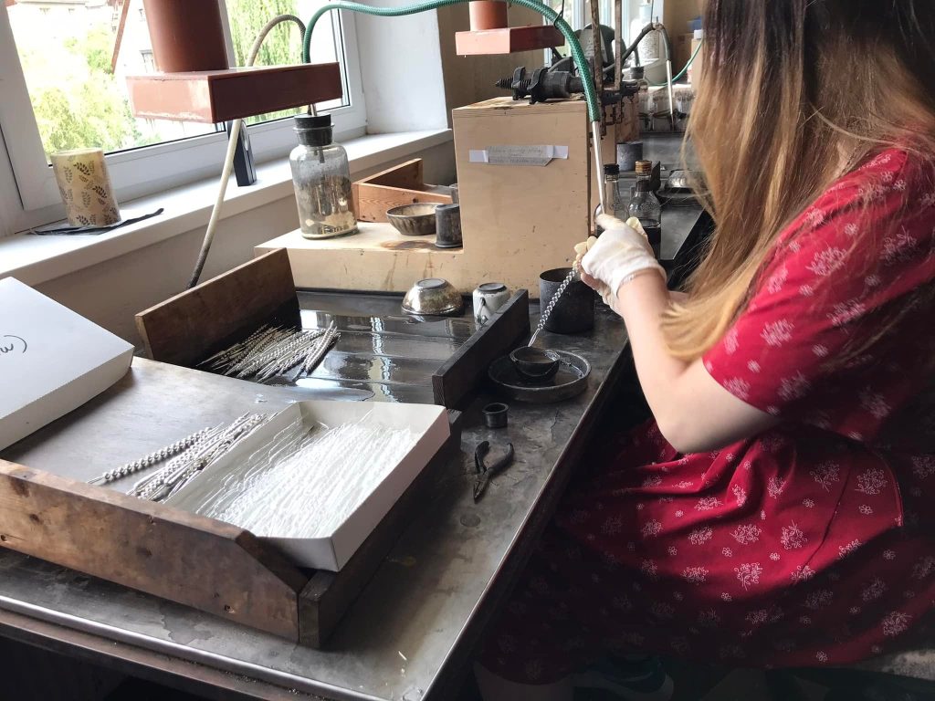 Herstellung von Glasschmuck. Mitarbeiterin führt es vor.